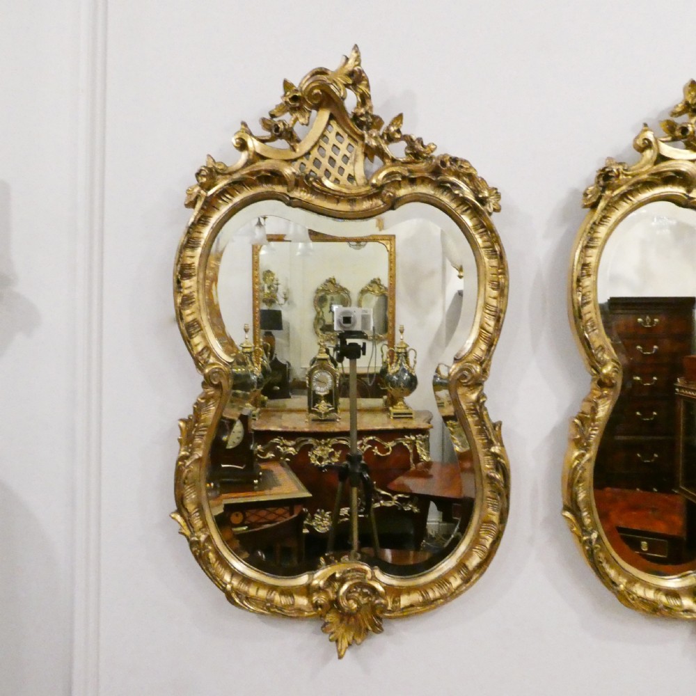 A pair of ornate French Rococo style wall mirrors featuring carved giltwood frames with scrollwork crests and lattice detailing. View II