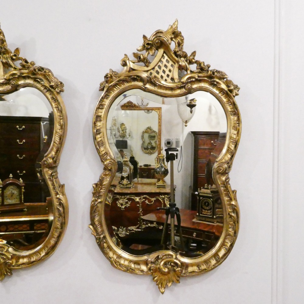 A pair of ornate French Rococo style wall mirrors featuring carved giltwood frames with scrollwork crests and lattice detailing. View III