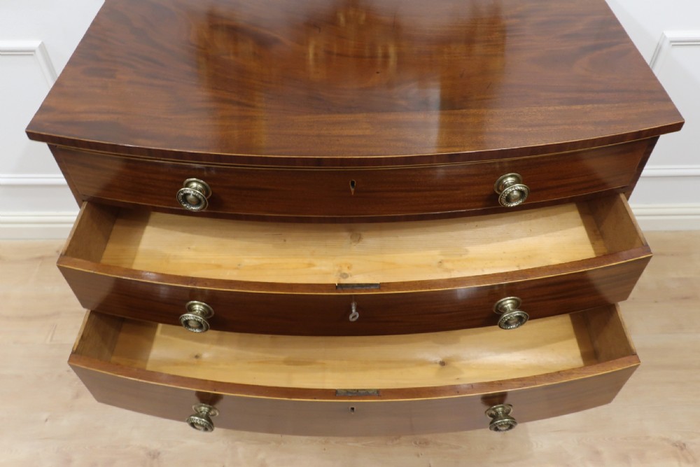 A Georgian mahogany bow-fronted chest of drawers featuring four graduated drawers with circular brass ring handles and splayed bracket feet. View IX
