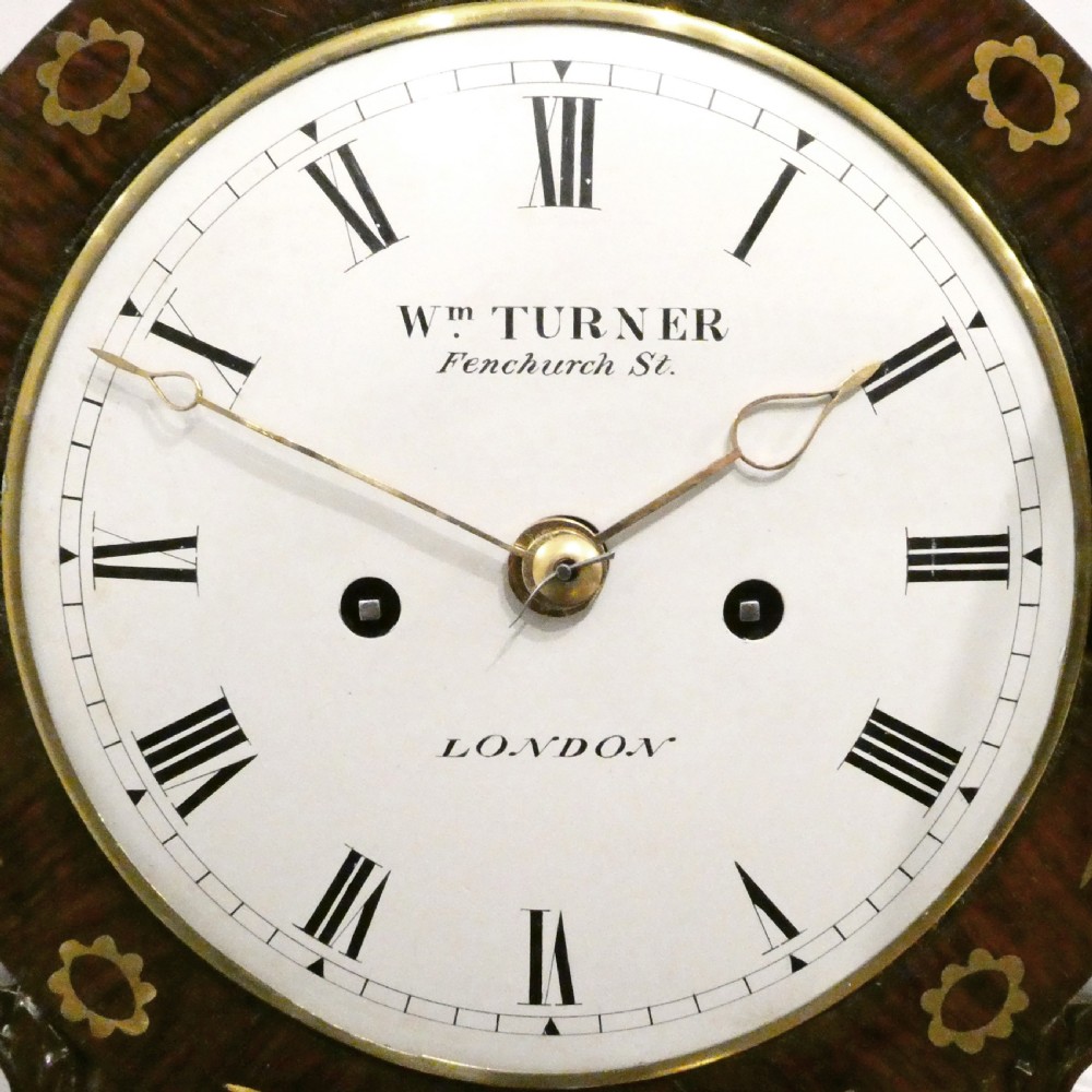 A Georgian rosewood bracket clock featuring intricate brass inlay, a brass pineapple finial, a white circular dial with Roman numerals, and brass ball feet. View II