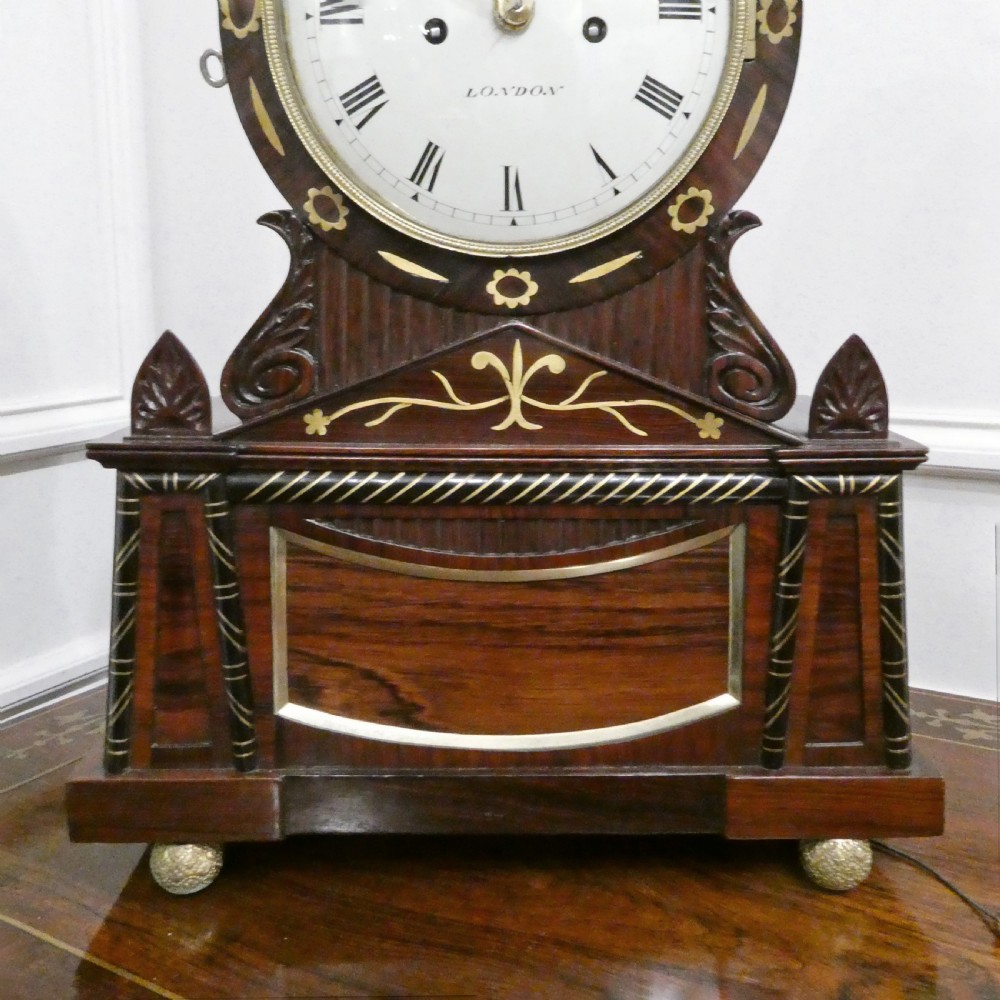 A Georgian rosewood bracket clock featuring intricate brass inlay, a brass pineapple finial, a white circular dial with Roman numerals, and brass ball feet. View III
