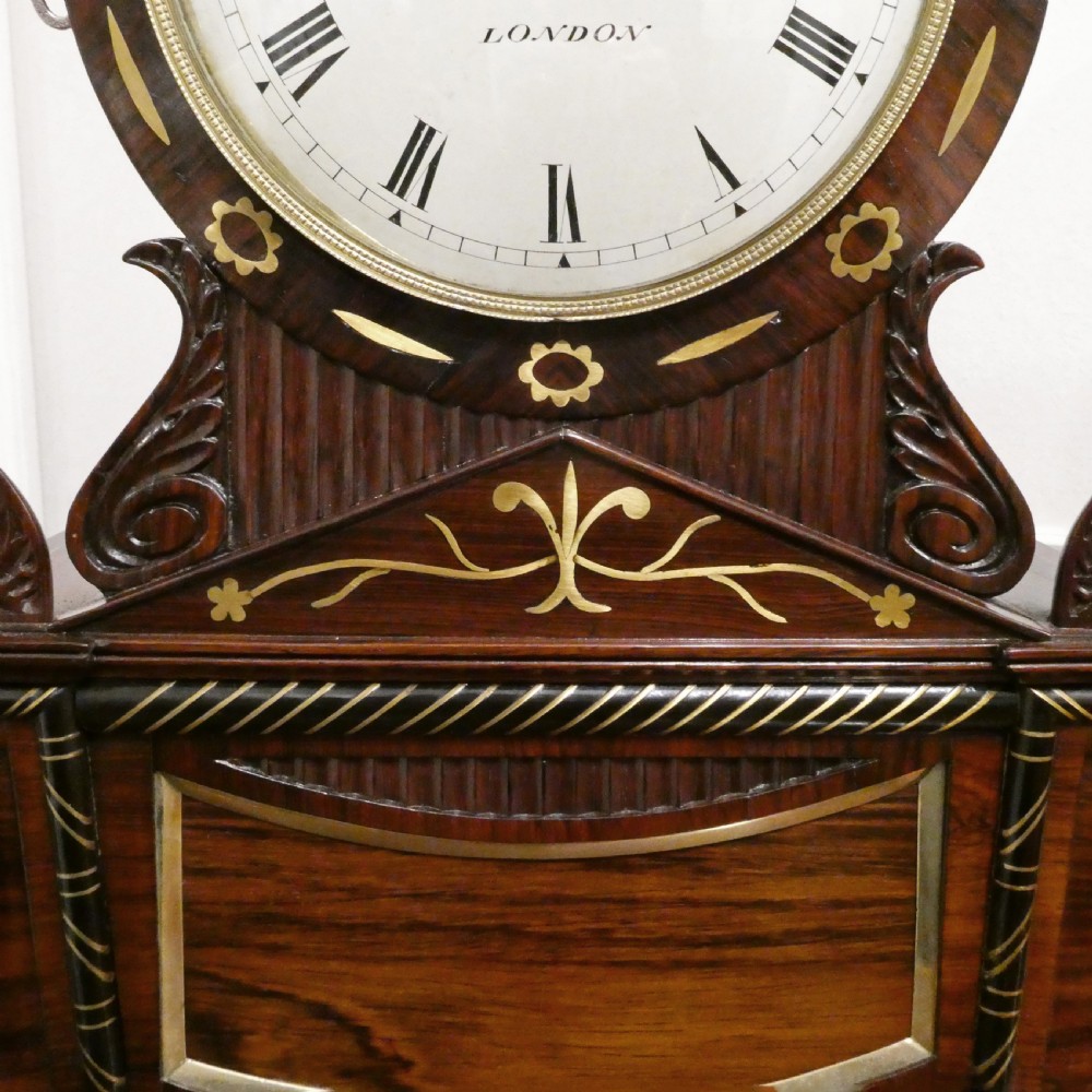A Georgian rosewood bracket clock featuring intricate brass inlay, a brass pineapple finial, a white circular dial with Roman numerals, and brass ball feet. View VI