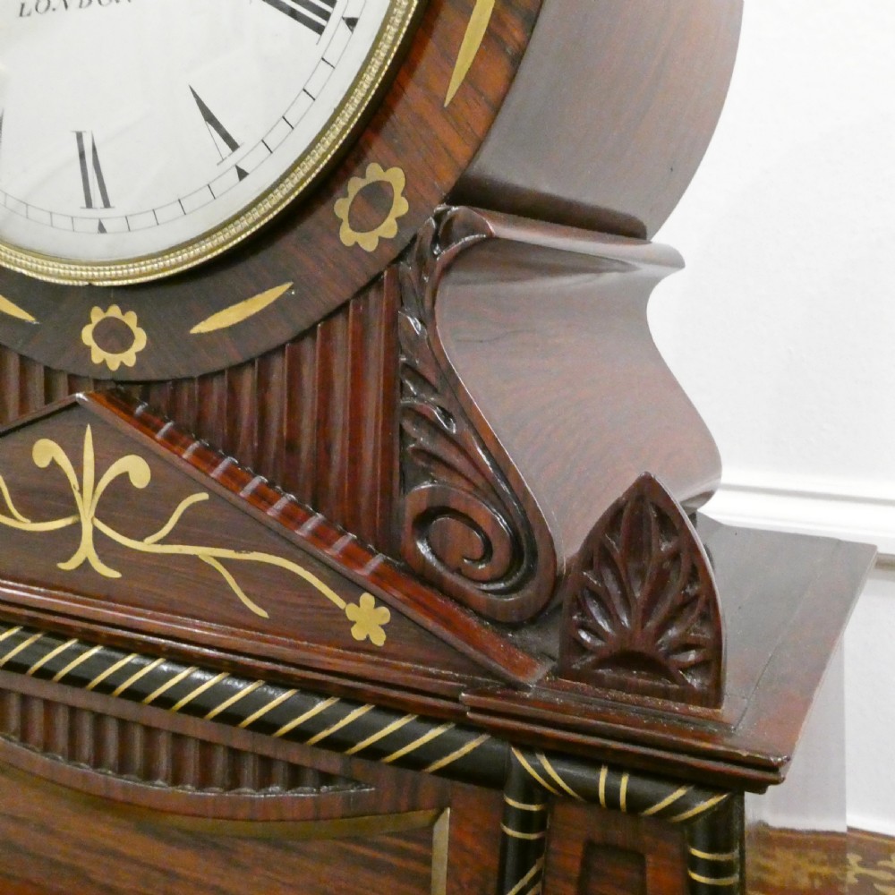 A Georgian rosewood bracket clock featuring intricate brass inlay, a brass pineapple finial, a white circular dial with Roman numerals, and brass ball feet. View VII