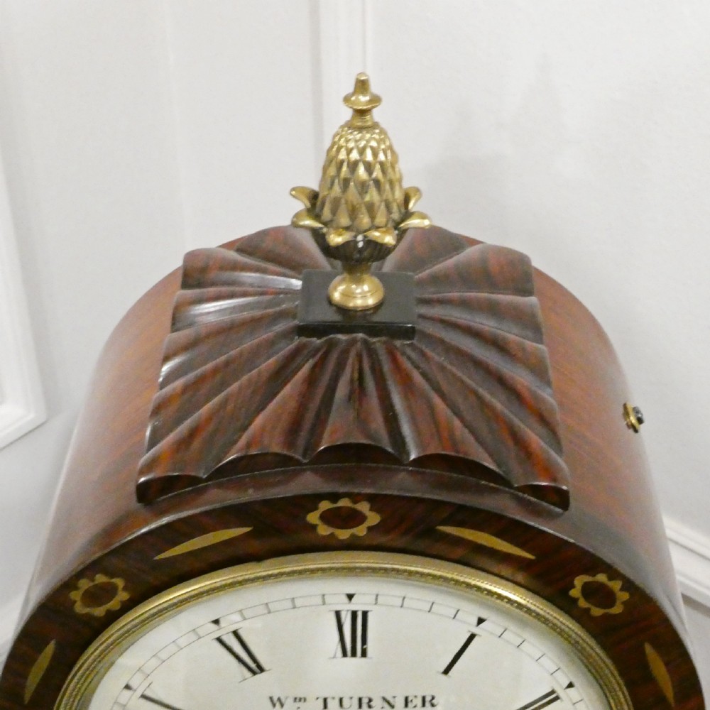 A Georgian rosewood bracket clock featuring intricate brass inlay, a brass pineapple finial, a white circular dial with Roman numerals, and brass ball feet. View VIII