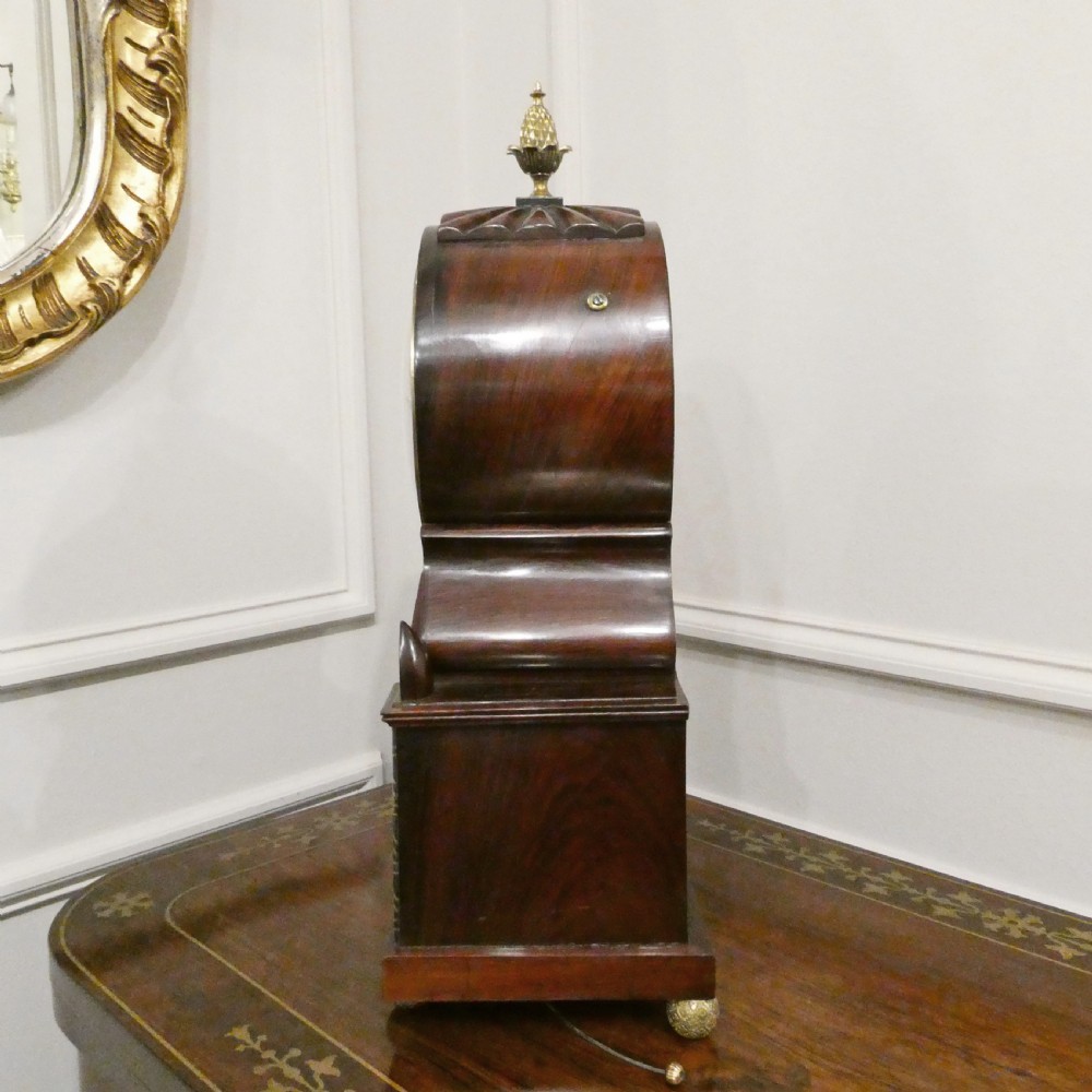 A Georgian rosewood bracket clock featuring intricate brass inlay, a brass pineapple finial, a white circular dial with Roman numerals, and brass ball feet. View IX