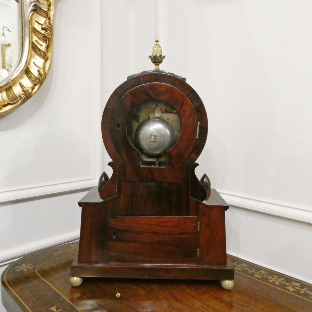 A Georgian rosewood bracket clock featuring intricate brass inlay, a brass pineapple finial, a white circular dial with Roman numerals, and brass ball feet. View X