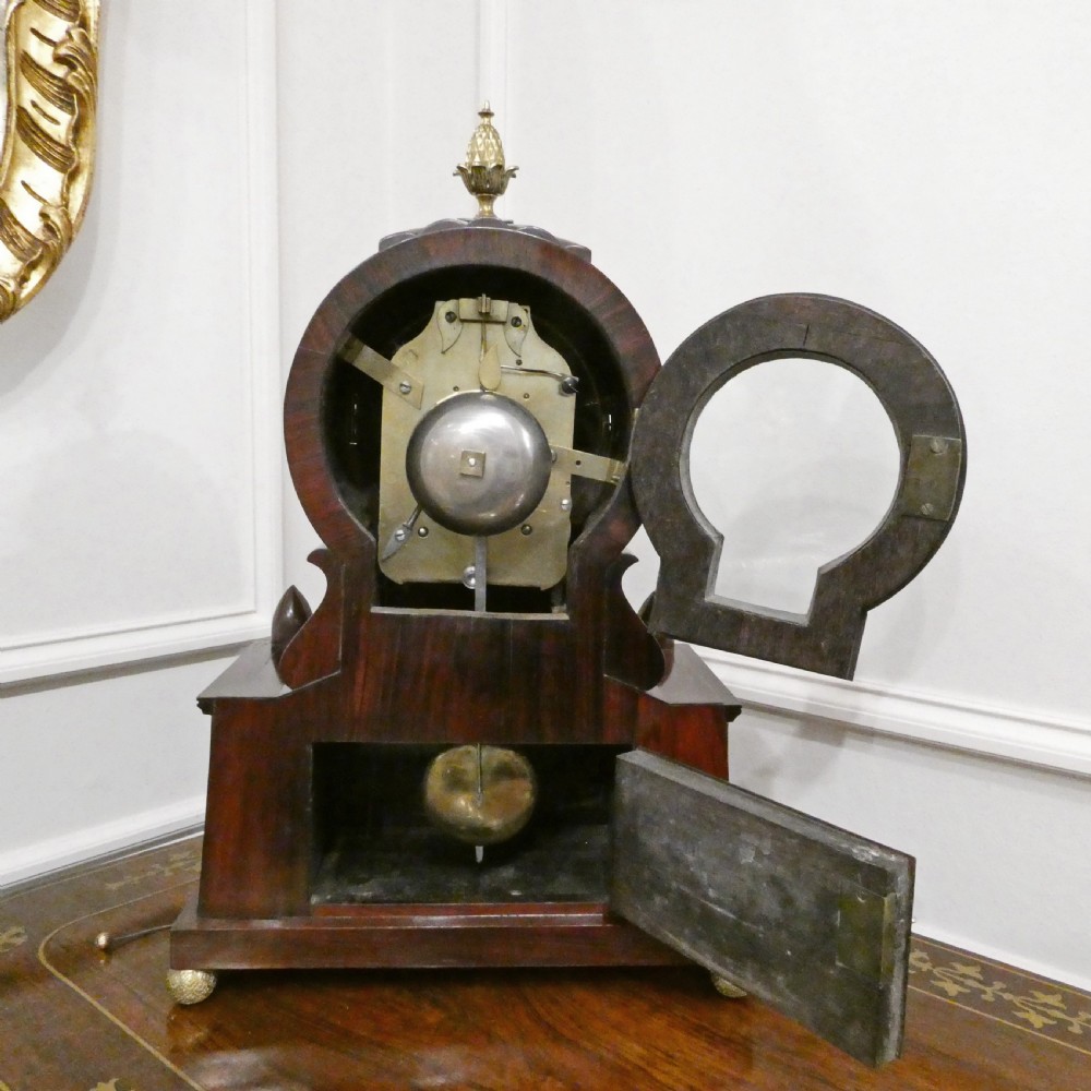 A Georgian rosewood bracket clock featuring intricate brass inlay, a brass pineapple finial, a white circular dial with Roman numerals, and brass ball feet. View XI