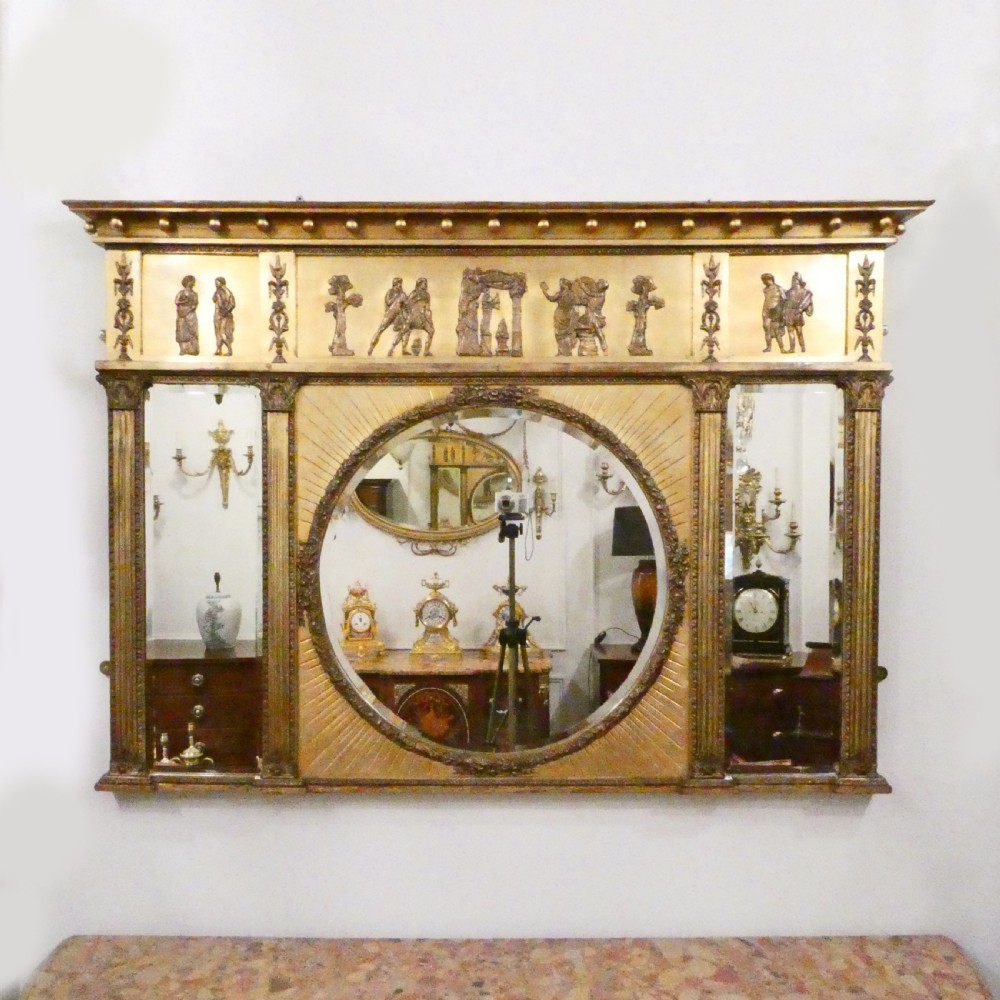 A rectangular giltwood overmantel wall mirror featuring a classical relief frieze above a central circular mirror plate flanked by two rectangular mirrored sections.