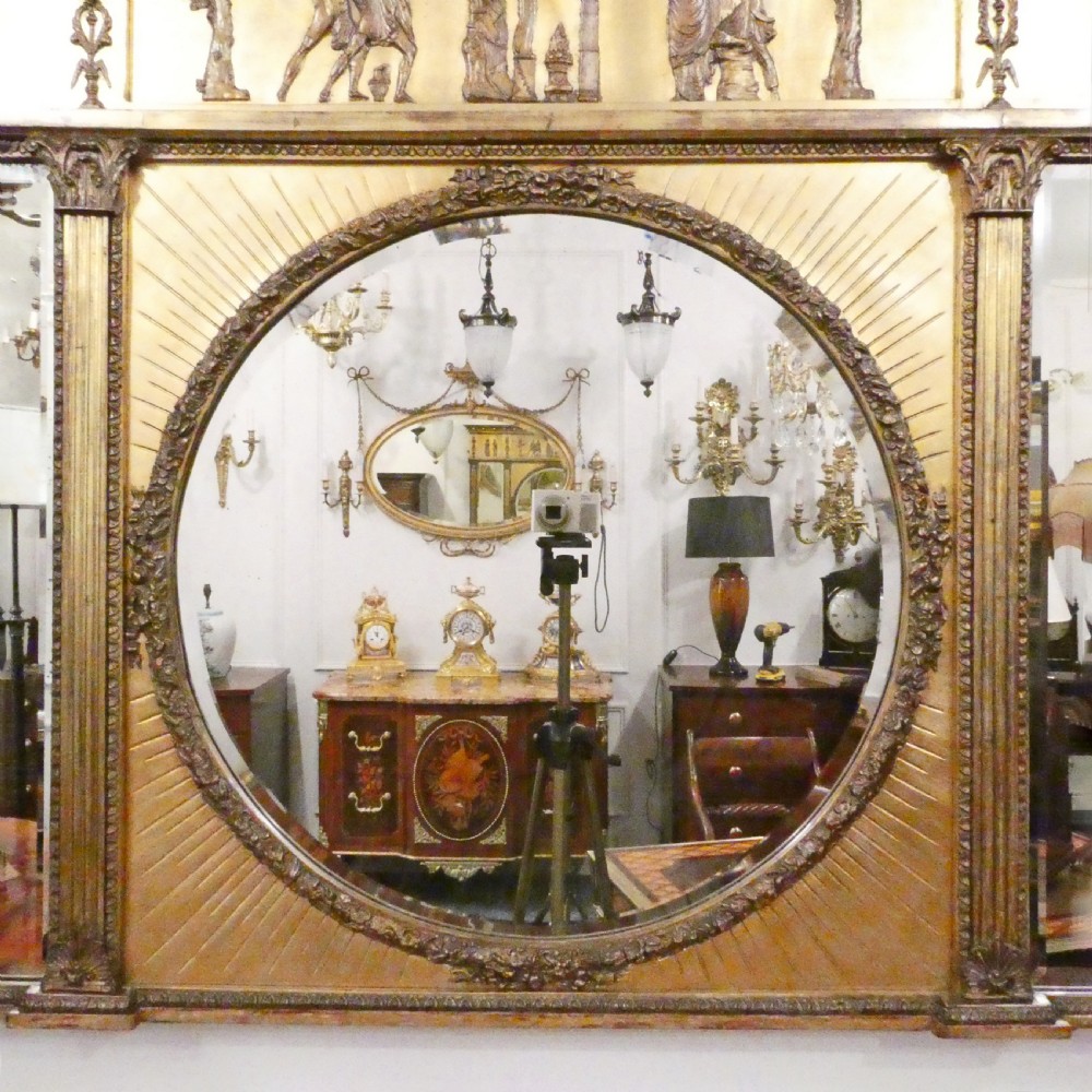 A rectangular giltwood overmantel wall mirror featuring a classical relief frieze above a central circular mirror plate flanked by two rectangular mirrored sections. View II