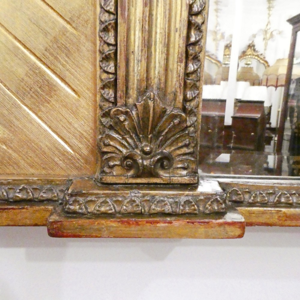 A rectangular giltwood overmantel wall mirror featuring a classical relief frieze above a central circular mirror plate flanked by two rectangular mirrored sections. View VI