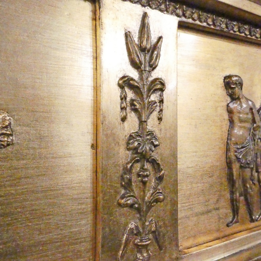A rectangular giltwood overmantel wall mirror featuring a classical relief frieze above a central circular mirror plate flanked by two rectangular mirrored sections. View XI