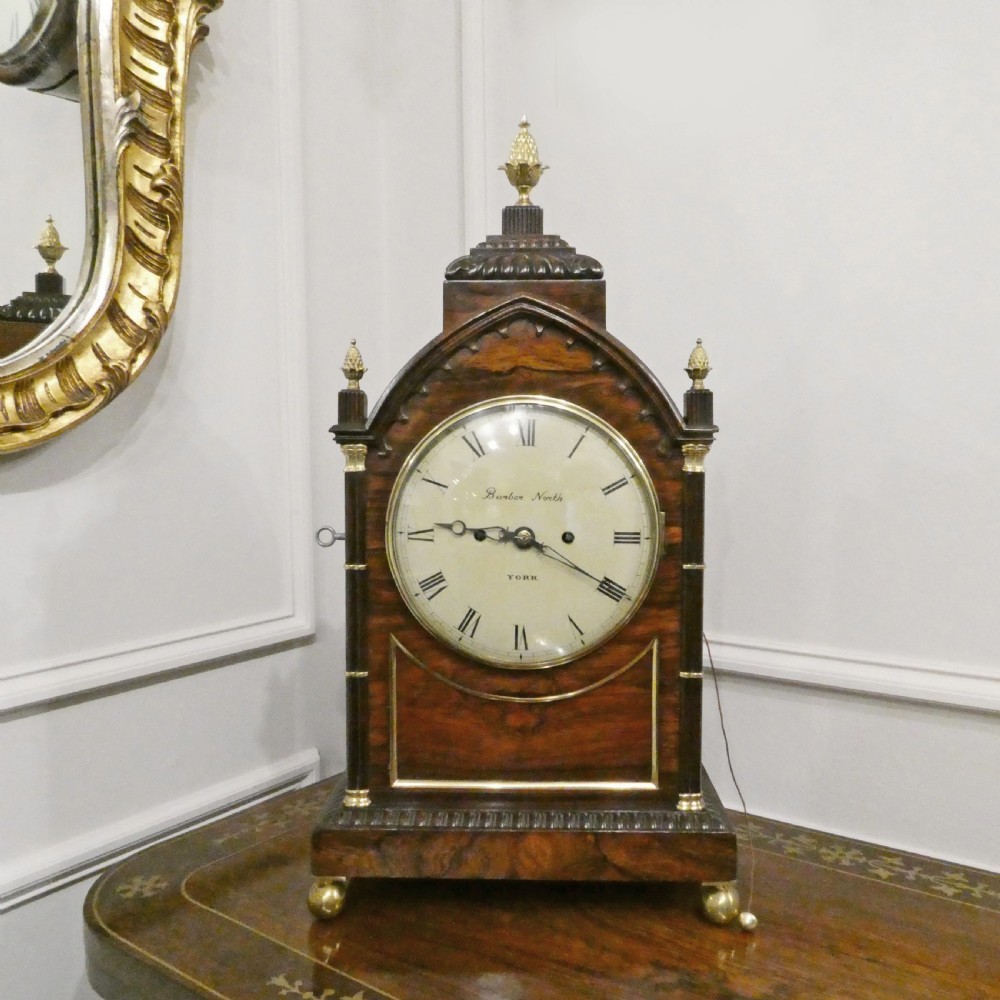 A dark rosewood William IV bracket clock featuring a gothic arch top, brass finials, brass feet, and a white dial signed Barber and North of York.