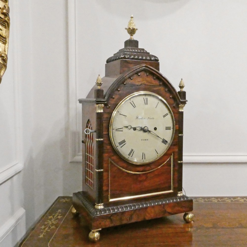 A dark rosewood William IV bracket clock featuring a gothic arch top, brass finials, brass feet, and a white dial signed Barber and North of York. View II