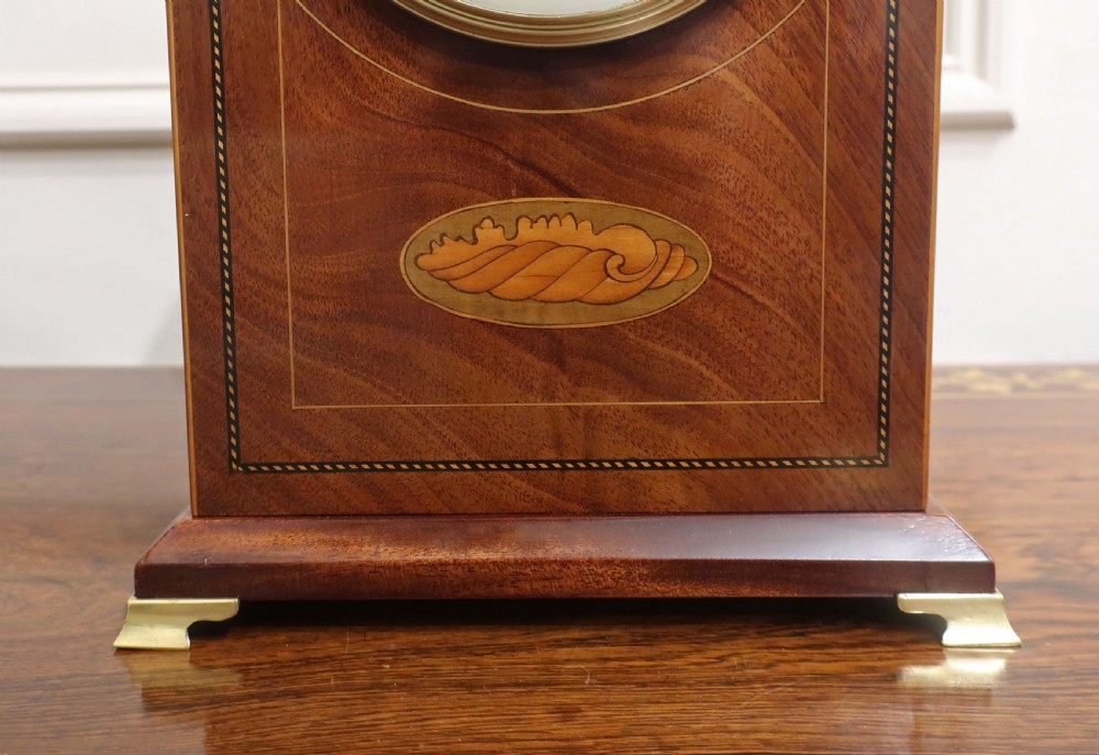 An arched French Belle Epoque mahogany mantel clock featuring fine string inlay, a central marquetry motif, a white dial with Arabic numerals, and small brass feet. View IV