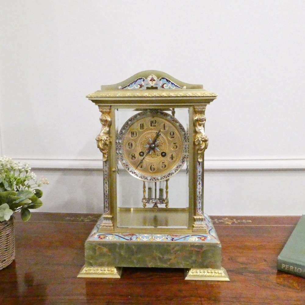 A late nineteenth-century French four-glass mantel clock featuring a green onyx base and top, champleve enamel borders, and a visible mercury pendulum.