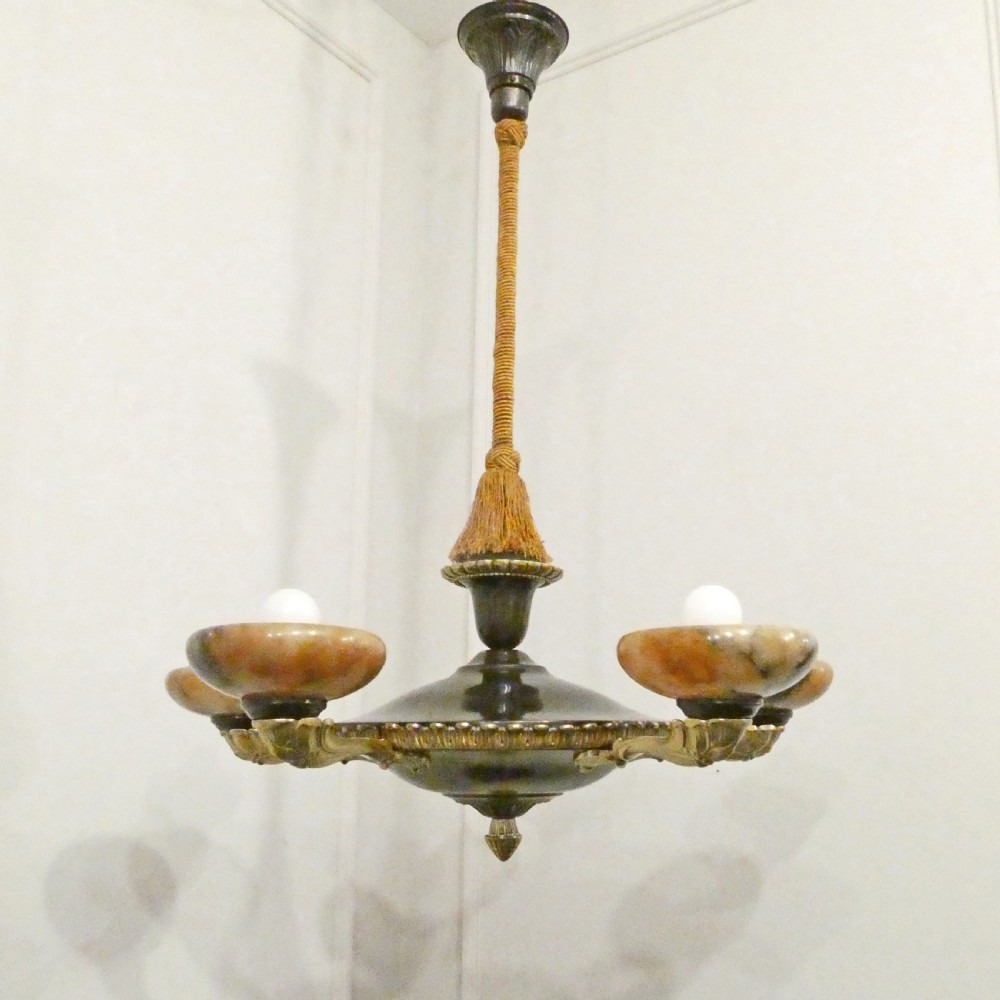An Art Deco bronze chandelier featuring carved alabaster shade cups suspended from a corded stem with decorative tassel detail.