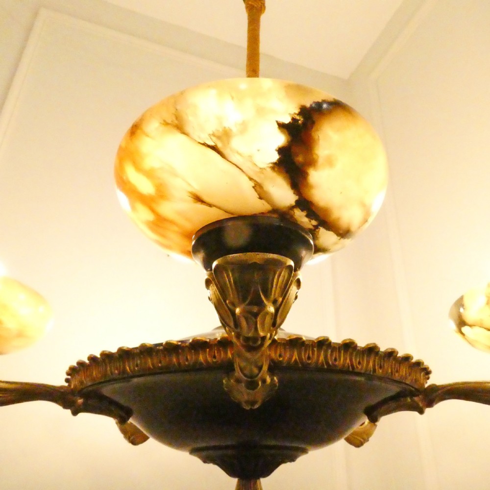 An Art Deco bronze chandelier featuring carved alabaster shade cups suspended from a corded stem with decorative tassel detail. View V