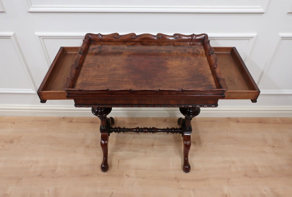 A Regency mahogany side table featuring a scalloped gallery tray top resting on turned end-supports with a central stretcher and splayed legs. View VII