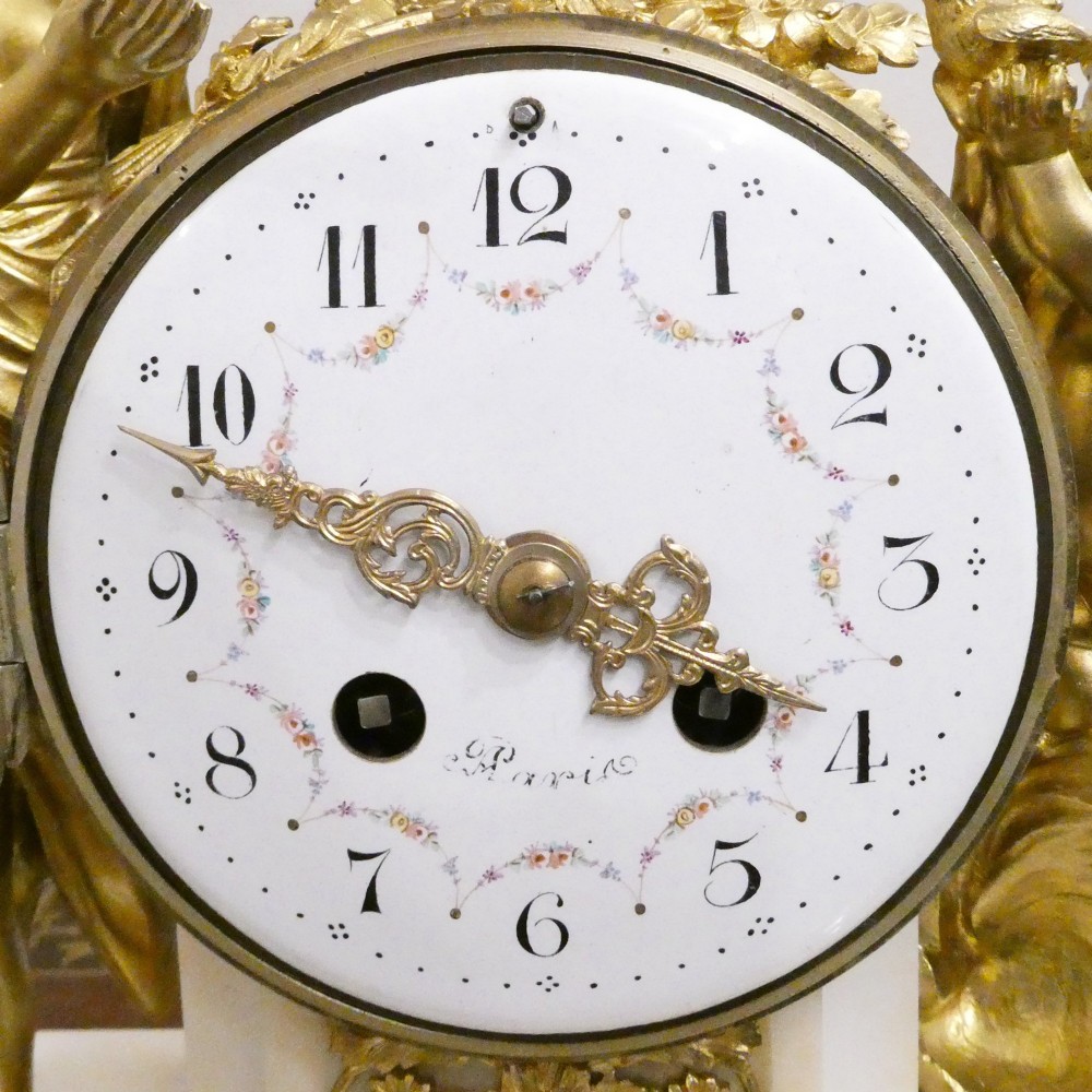 A French Louis XVI style gilt bronze and white marble mantel clock featuring classical female and winged cherub figures surrounding a white enamel dial. View II
