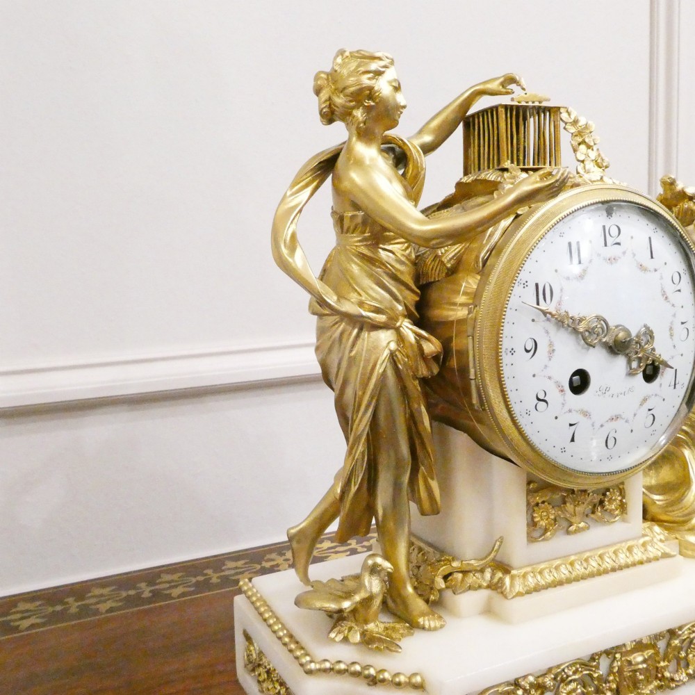 A French Louis XVI style gilt bronze and white marble mantel clock featuring classical female and winged cherub figures surrounding a white enamel dial. View IV