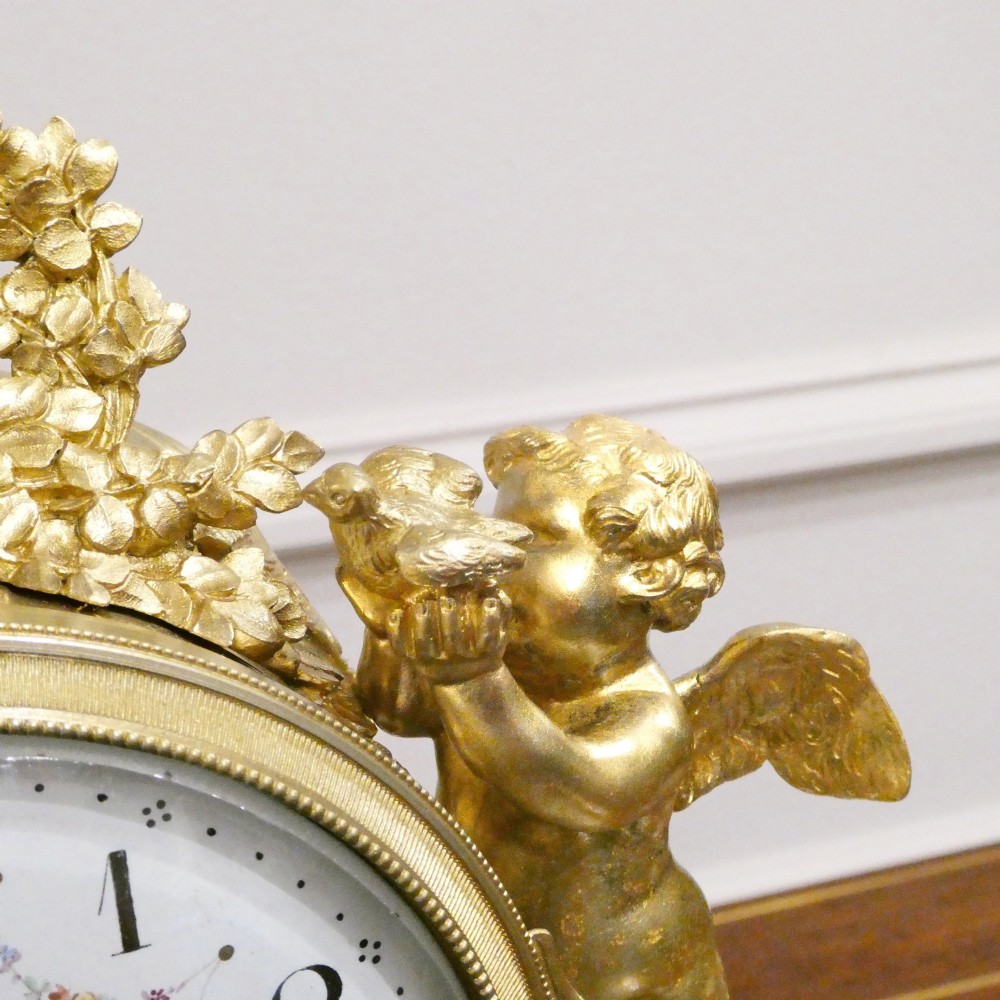 A French Louis XVI style gilt bronze and white marble mantel clock featuring classical female and winged cherub figures surrounding a white enamel dial. View V