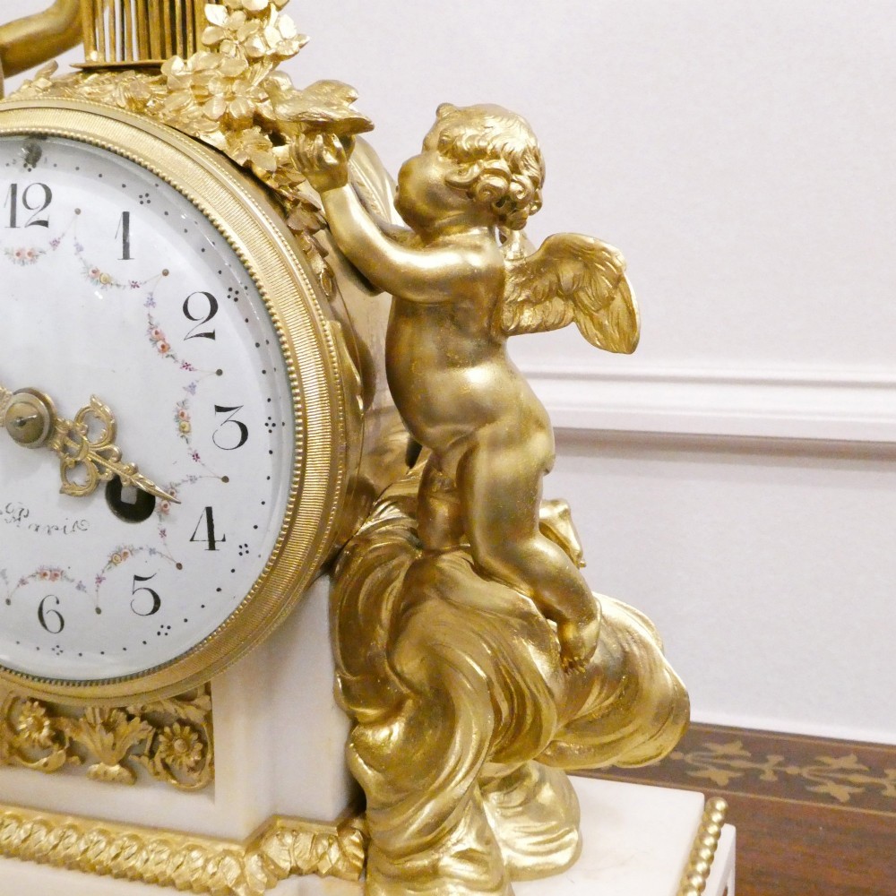 A French Louis XVI style gilt bronze and white marble mantel clock featuring classical female and winged cherub figures surrounding a white enamel dial. View VI