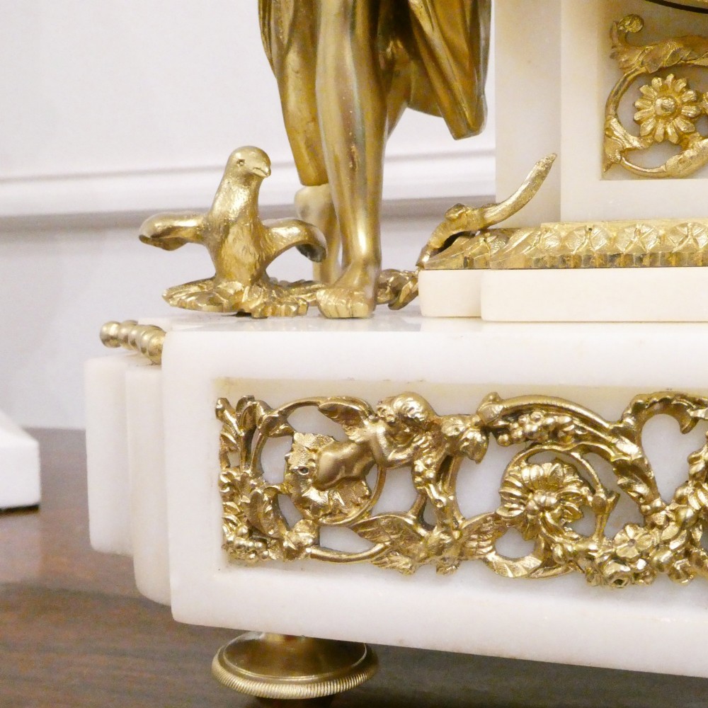 A French Louis XVI style gilt bronze and white marble mantel clock featuring classical female and winged cherub figures surrounding a white enamel dial. View VIII