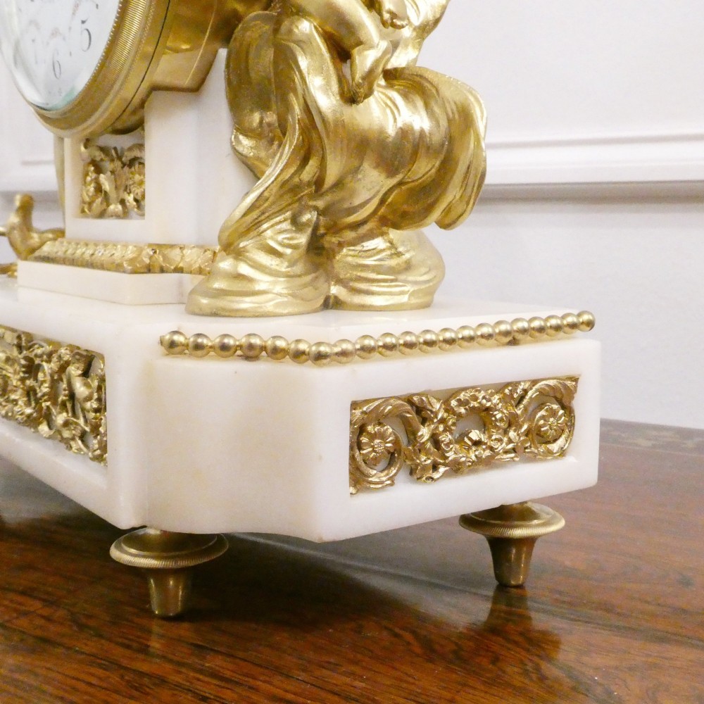 A French Louis XVI style gilt bronze and white marble mantel clock featuring classical female and winged cherub figures surrounding a white enamel dial. View IX