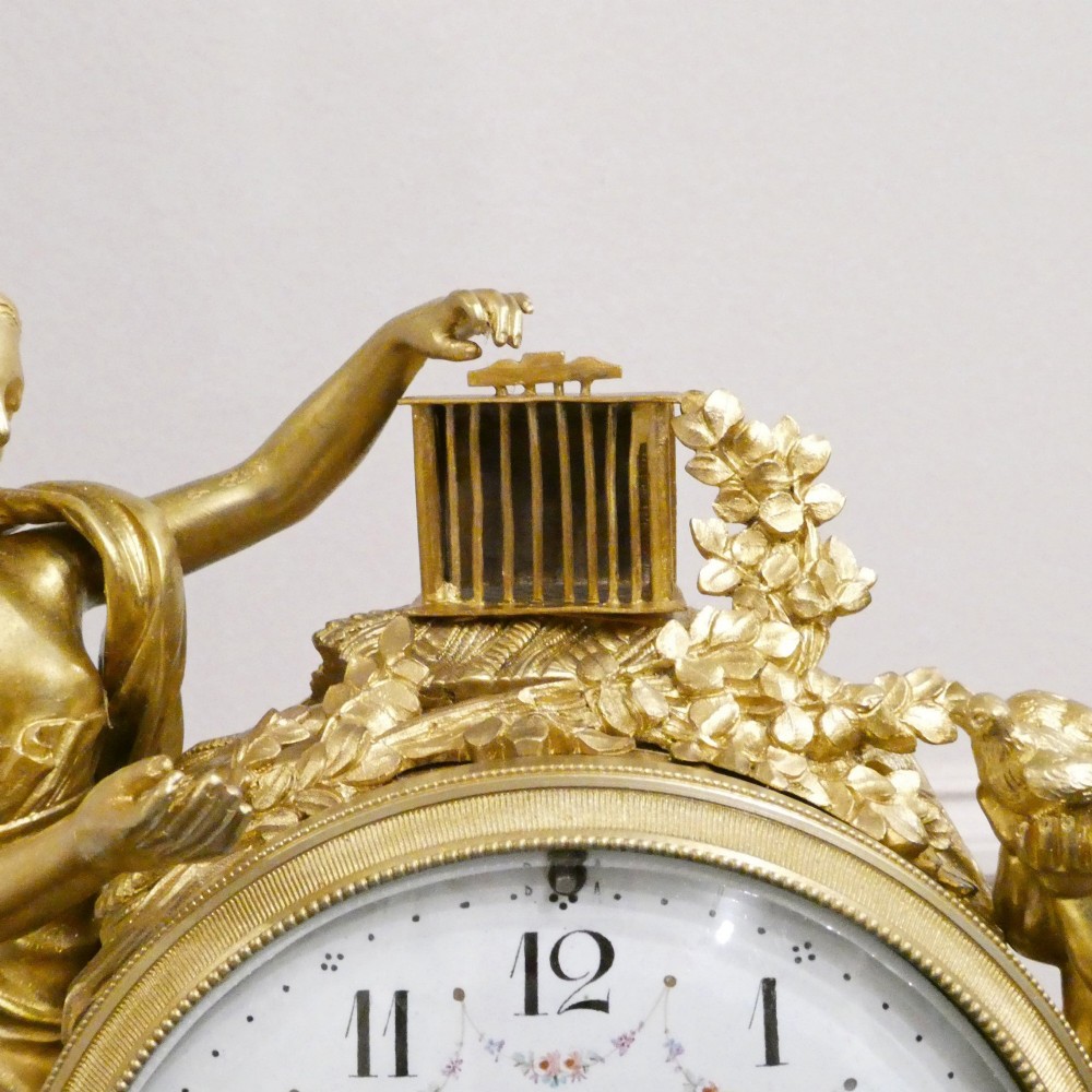A French Louis XVI style gilt bronze and white marble mantel clock featuring classical female and winged cherub figures surrounding a white enamel dial. View X