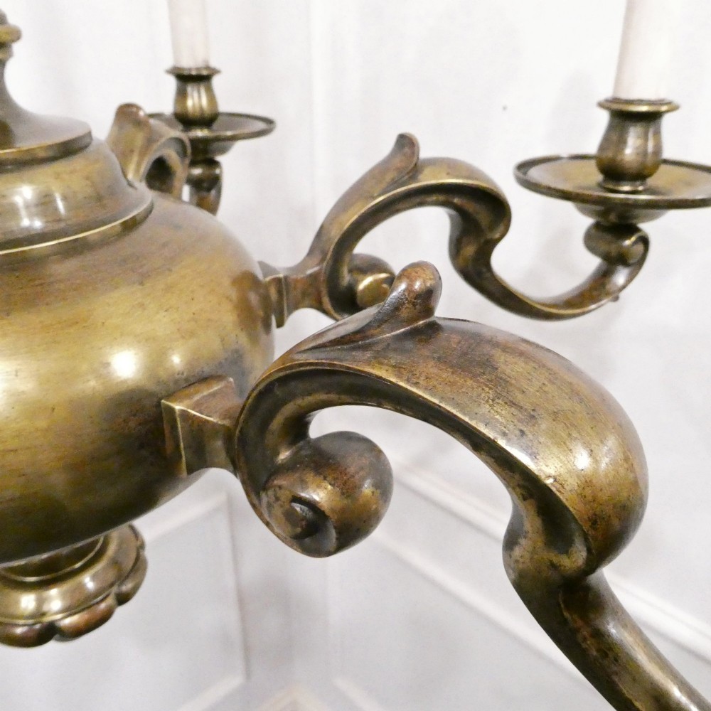 An Edwardian six-light aged brass chandelier featuring a central turned baluster shaft, scrolled arms, and candle sleeves. View VI