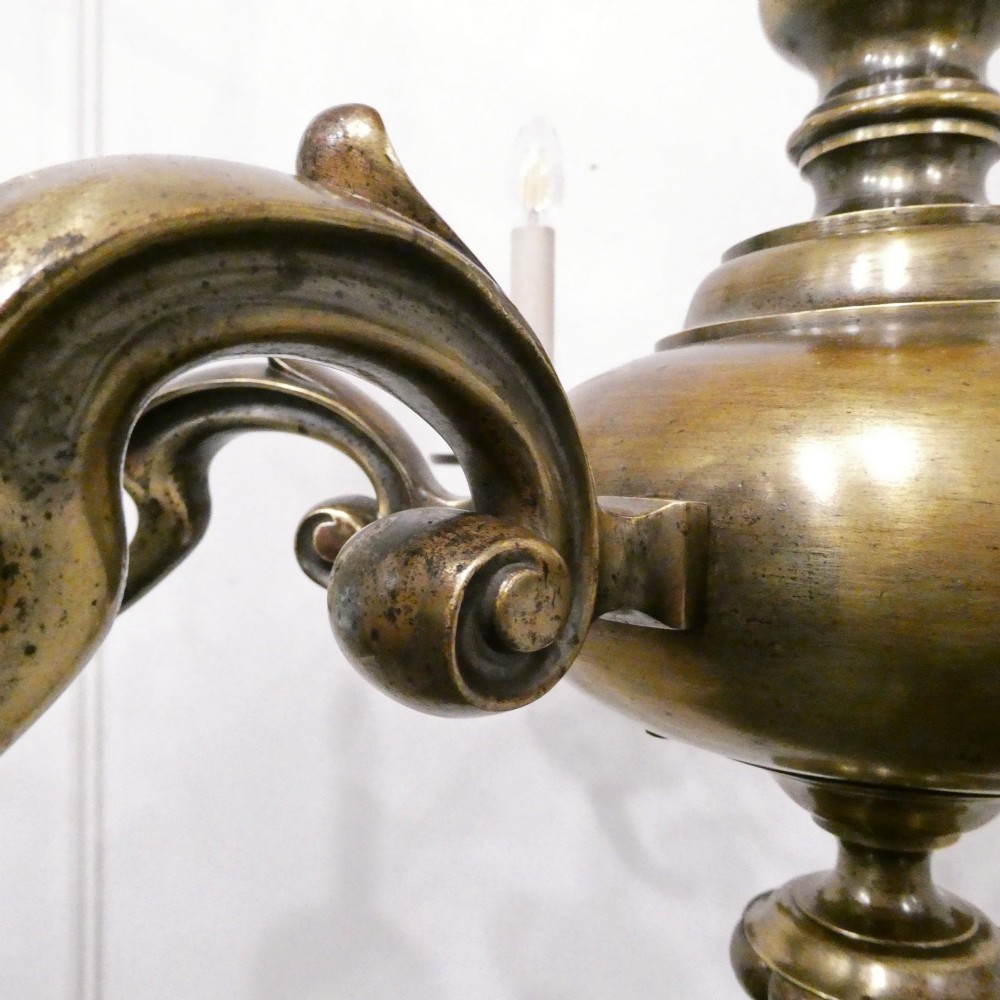 An Edwardian six-light aged brass chandelier featuring a central turned baluster shaft, scrolled arms, and candle sleeves. View VII