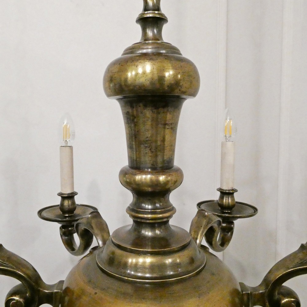 An Edwardian six-light aged brass chandelier featuring a central turned baluster shaft, scrolled arms, and candle sleeves. View IX