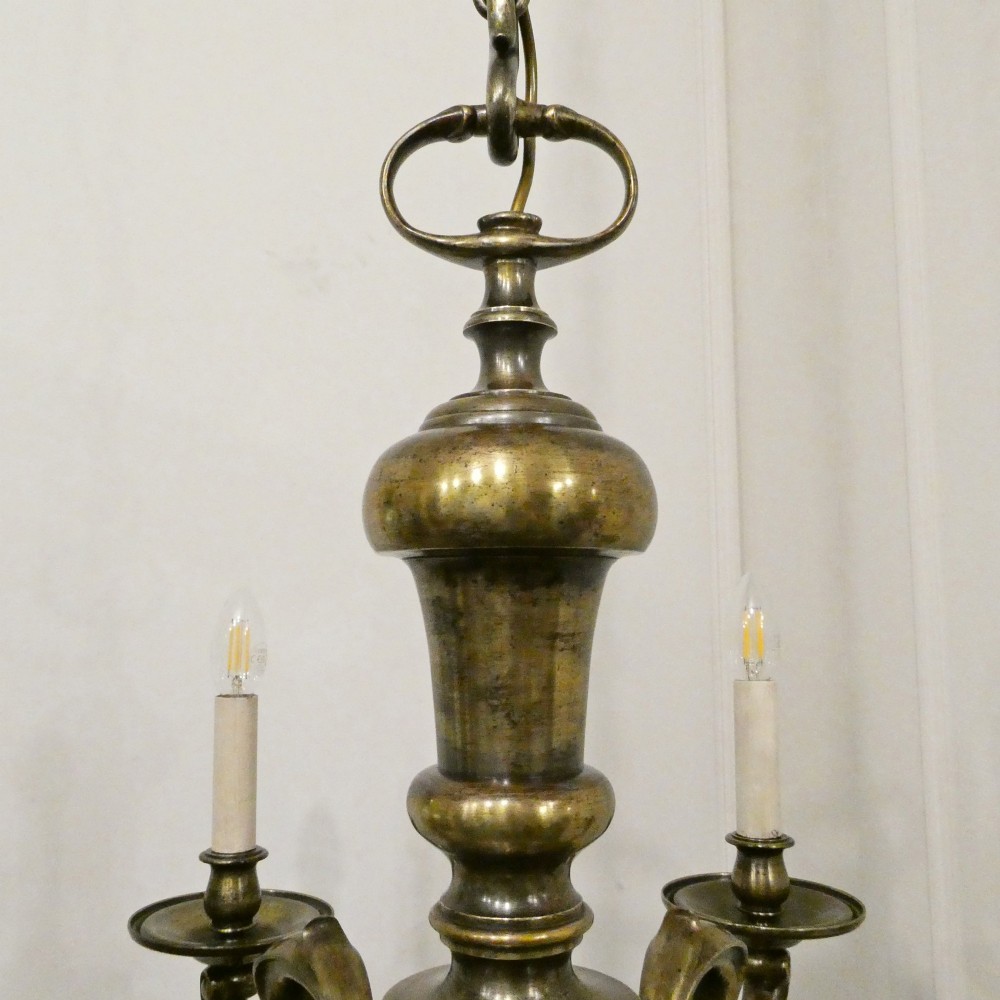 An Edwardian six-light aged brass chandelier featuring a central turned baluster shaft, scrolled arms, and candle sleeves. View X