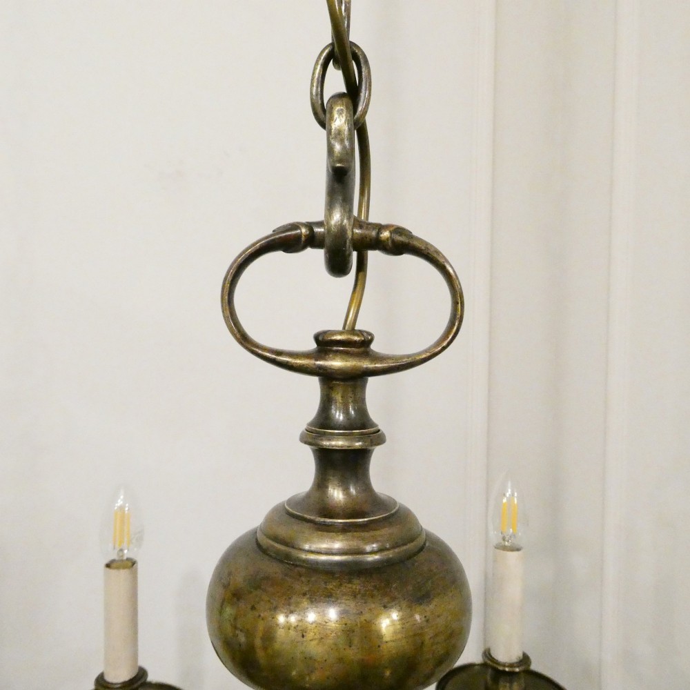 An Edwardian six-light aged brass chandelier featuring a central turned baluster shaft, scrolled arms, and candle sleeves. View XII