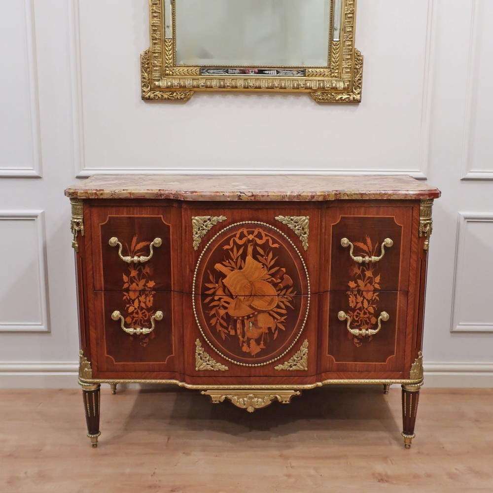 A French Louis XVI style marquetry chest of drawers featuring inlaid central medallion motifs, gilded bronze handles, tapered legs, and a fitted marble top.