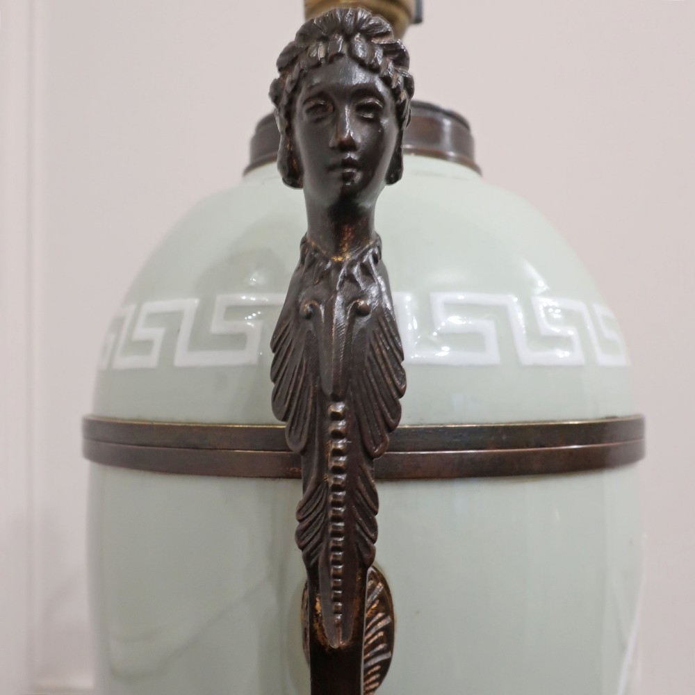 A French Neoclassical style table lamp featuring a pale green pate-sur-pate porcelain urn base, dark bronze side handles, and a pleated cream shade. View IX