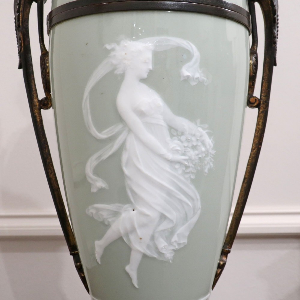 A French Neoclassical style table lamp featuring a pale green pate-sur-pate porcelain urn base, dark bronze side handles, and a pleated cream shade. View XIV