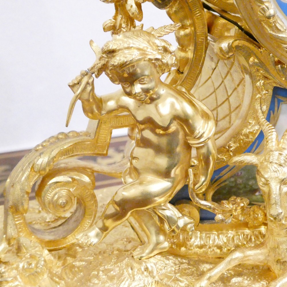 An ornate antique French gilt bronze mantel clock featuring decorative cherub figures, a recumbent goat sculpture, and blue porcelain panels painted with cherubs and floral motifs. View V