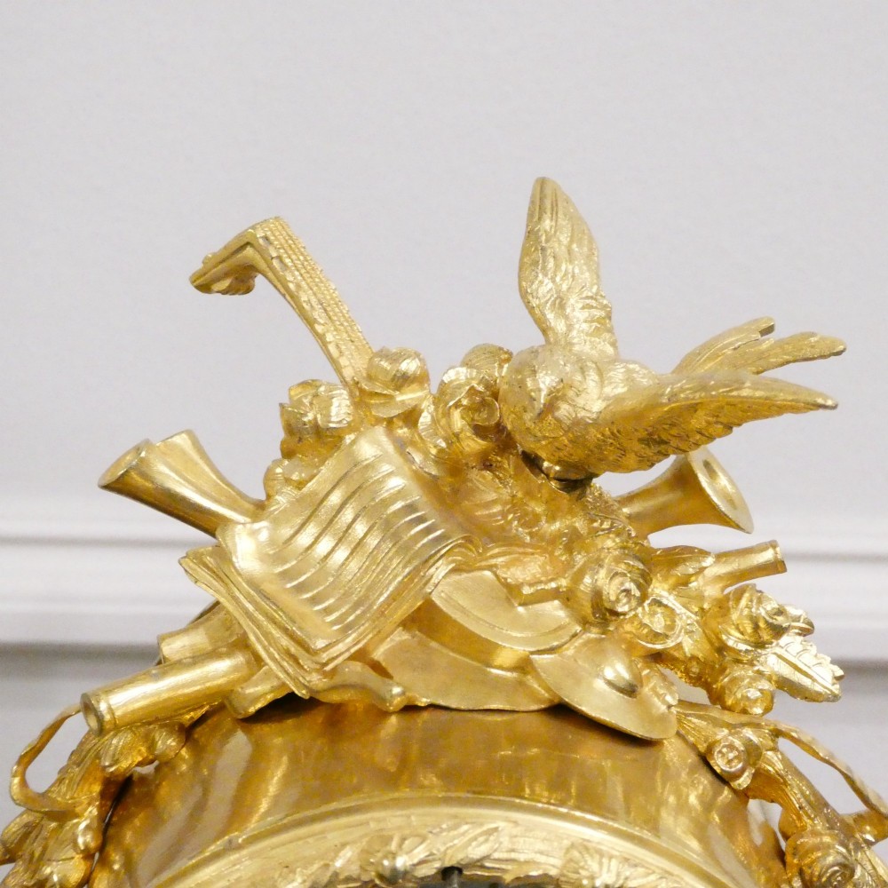 An ornate antique French gilt bronze mantel clock featuring decorative cherub figures, a recumbent goat sculpture, and blue porcelain panels painted with cherubs and floral motifs. View VII