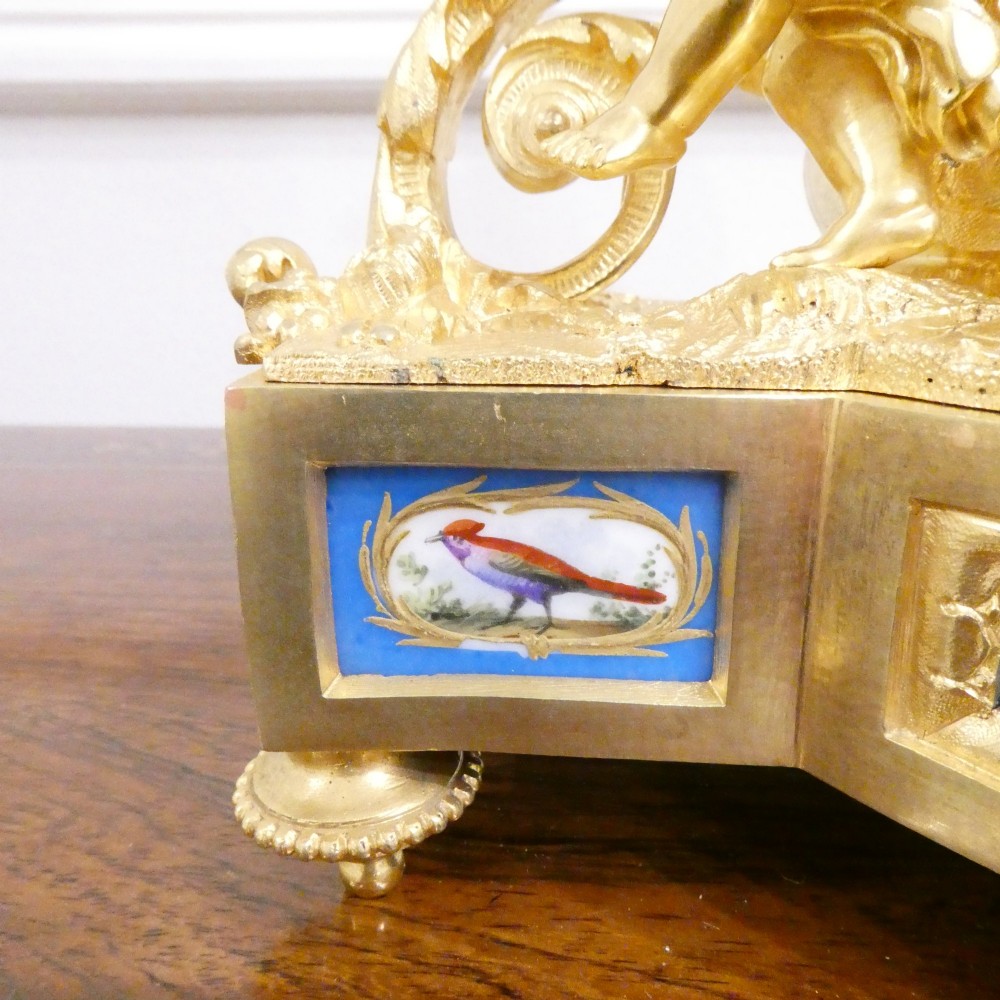 An ornate antique French gilt bronze mantel clock featuring decorative cherub figures, a recumbent goat sculpture, and blue porcelain panels painted with cherubs and floral motifs. View VIII