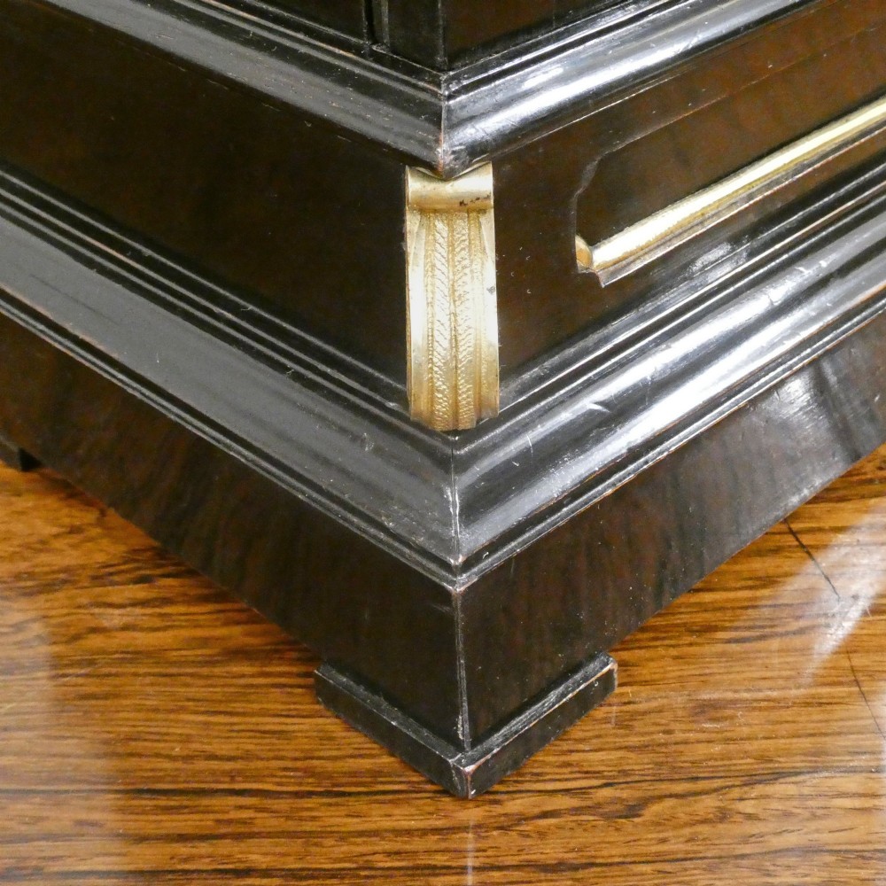 An early Victorian ebonised wooden library clock featuring a square dial with Roman numerals, side viewing apertures, and brass accents. View VI