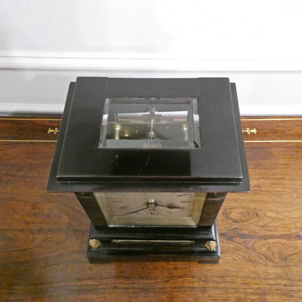 An early Victorian ebonised wooden library clock featuring a square dial with Roman numerals, side viewing apertures, and brass accents. View VII