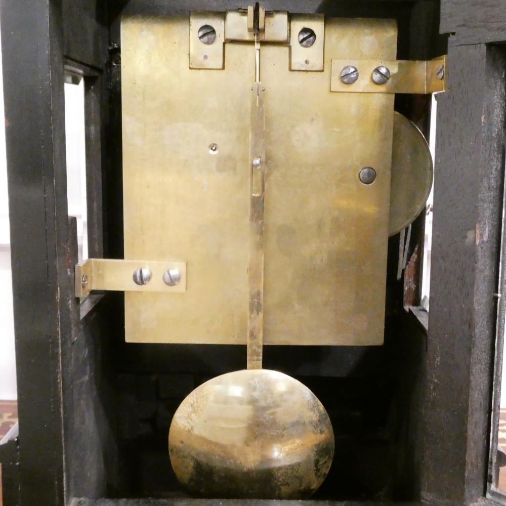 An early Victorian ebonised wooden library clock featuring a square dial with Roman numerals, side viewing apertures, and brass accents. View XII