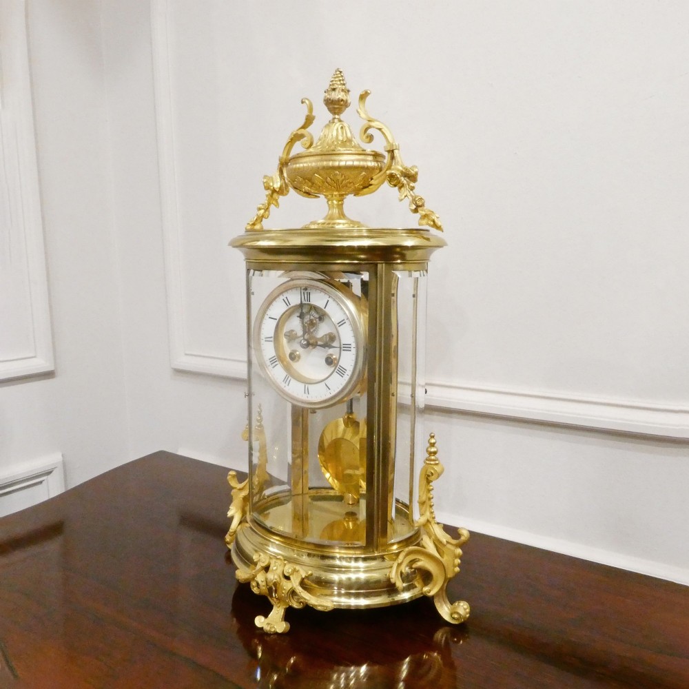 A French gilt bronze and brass four-glass mantel clock featuring an urn finial, visible pendulum mechanism, and white enamel dial with Roman numerals. View II