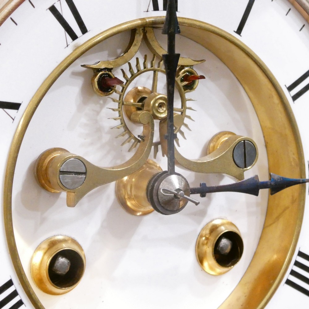 A French gilt bronze and brass four-glass mantel clock featuring an urn finial, visible pendulum mechanism, and white enamel dial with Roman numerals. View IV