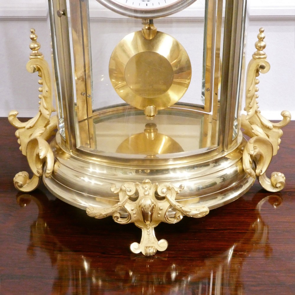 A French gilt bronze and brass four-glass mantel clock featuring an urn finial, visible pendulum mechanism, and white enamel dial with Roman numerals. View V