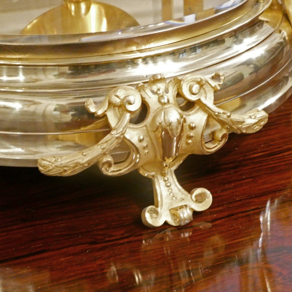 A French gilt bronze and brass four-glass mantel clock featuring an urn finial, visible pendulum mechanism, and white enamel dial with Roman numerals. View VI