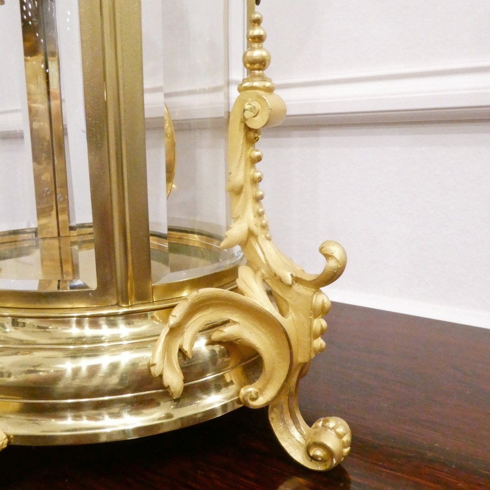 A French gilt bronze and brass four-glass mantel clock featuring an urn finial, visible pendulum mechanism, and white enamel dial with Roman numerals. View VII