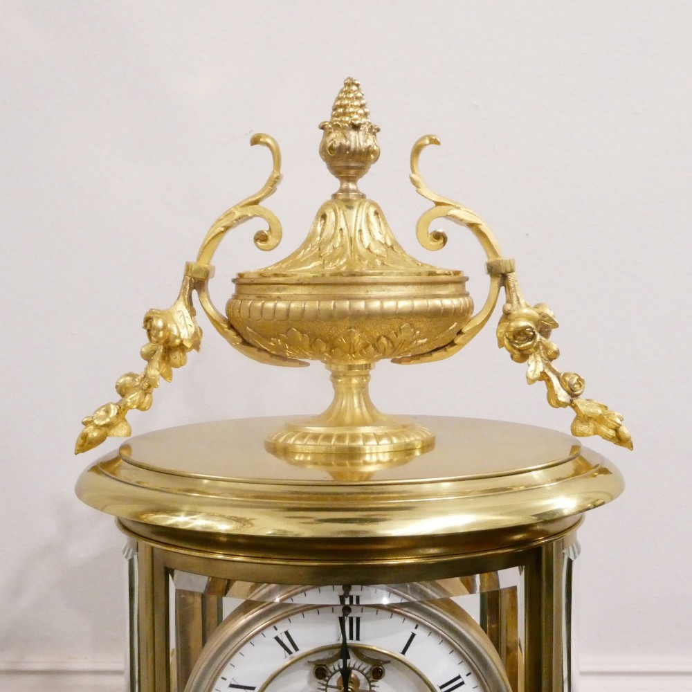 A French gilt bronze and brass four-glass mantel clock featuring an urn finial, visible pendulum mechanism, and white enamel dial with Roman numerals. View VIII