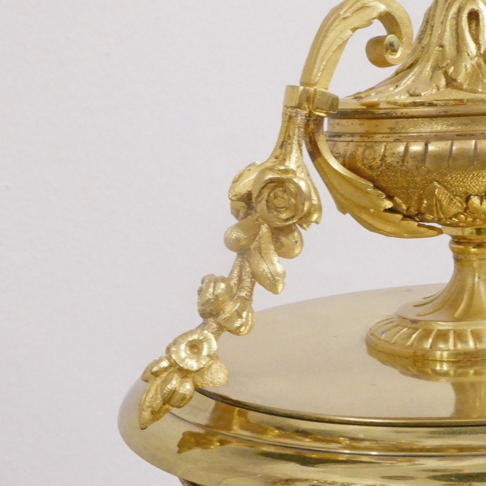 A French gilt bronze and brass four-glass mantel clock featuring an urn finial, visible pendulum mechanism, and white enamel dial with Roman numerals. View X